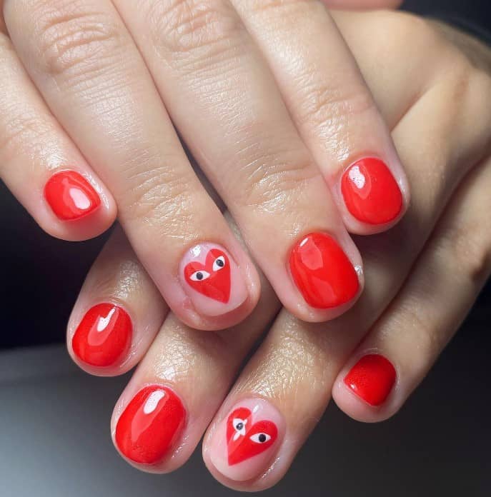 A woman's bright red manicure with nude accent nails decorated with the Comme Des Garçons’ play heart logo nail art