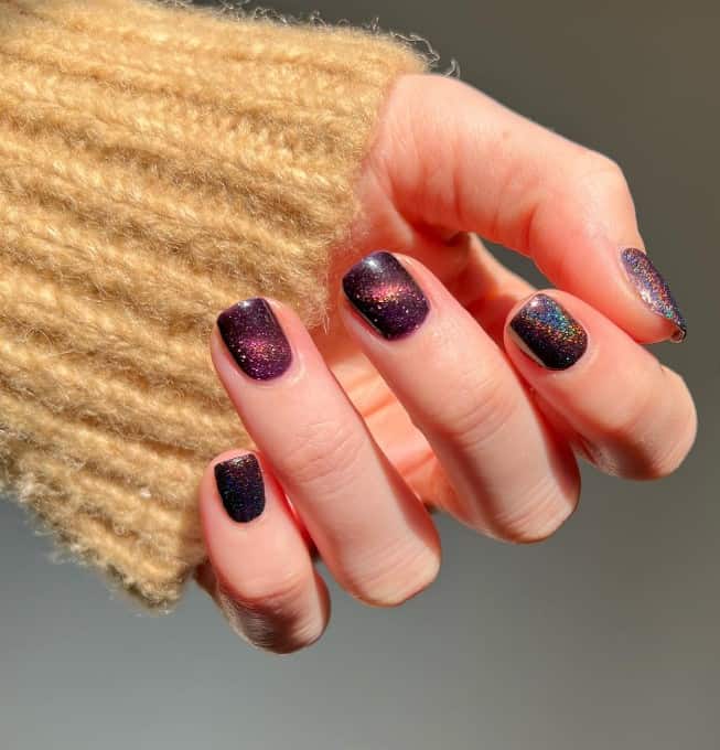 A woman's hand with dark purple cat-eye nails and topped with holographic design