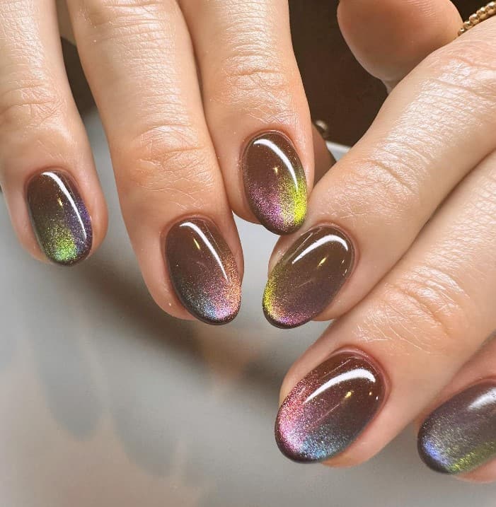 A woman's hands with a brown colored manicure where a hypnotic play of shimmering colors forms a cat-eye pattern on the tips.