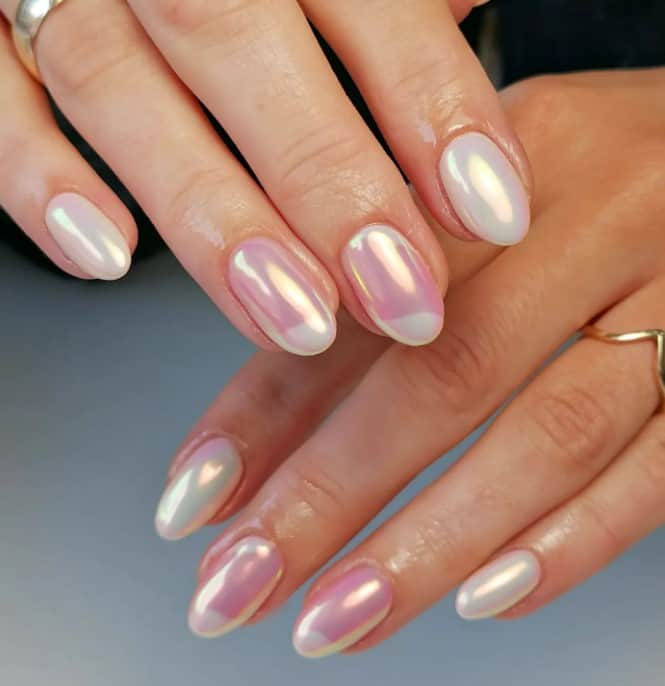 A woman's hands with glazed donut nails by pairing pearlescent white nails with pink chrome nails in the middle, featuring swirly half-white French tips accents