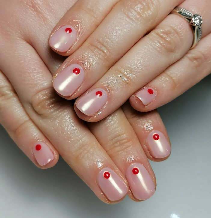 A woman's hands with red dots on the cuticles of nude-pink base