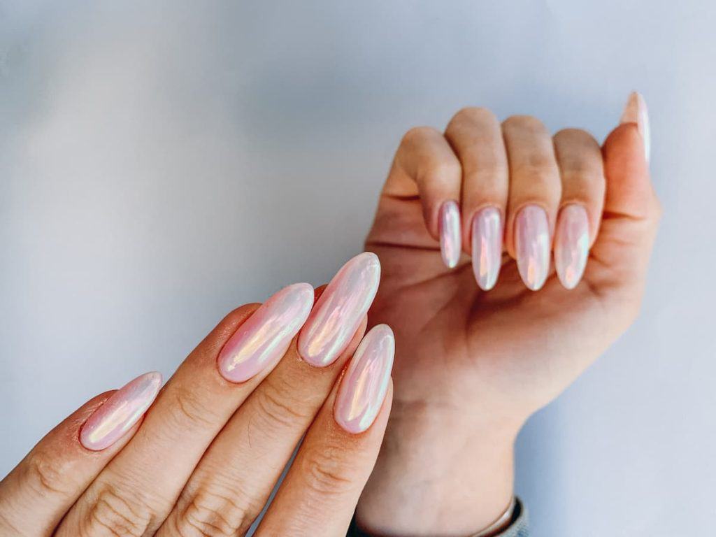 A woman's hands with pink holographic nails on a white background.