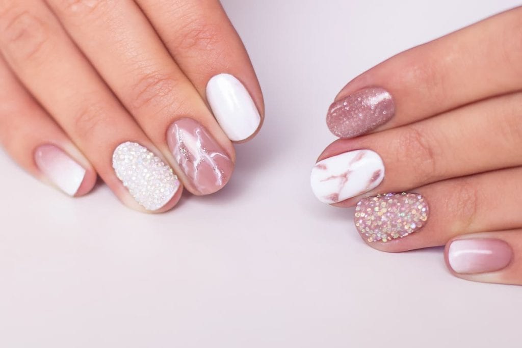A woman's hands with pink and white manicures with a marble effect, gradient and sparkle designs
