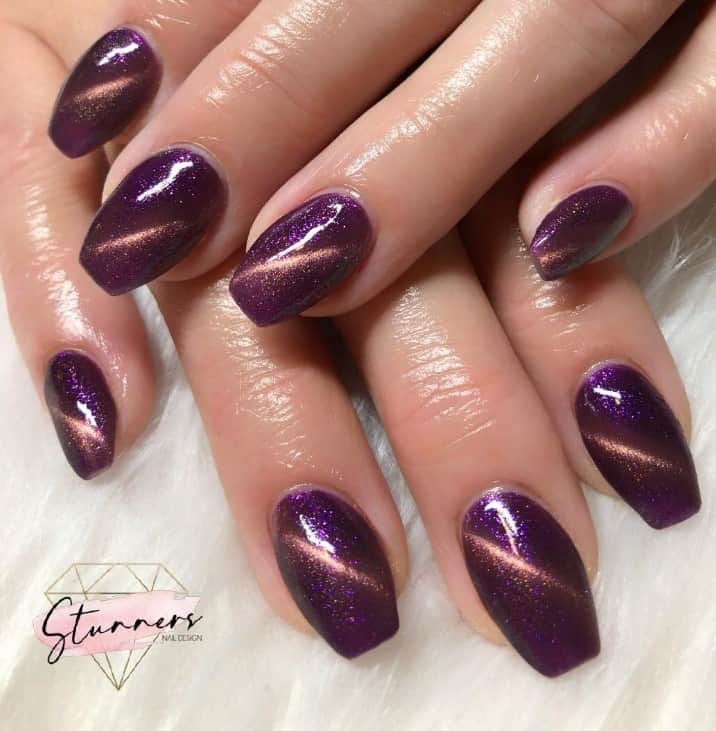 A woman's dark purple base and gold magnetic polish weaving an elegant diagonal pattern mimics the eyes of a majestic cat