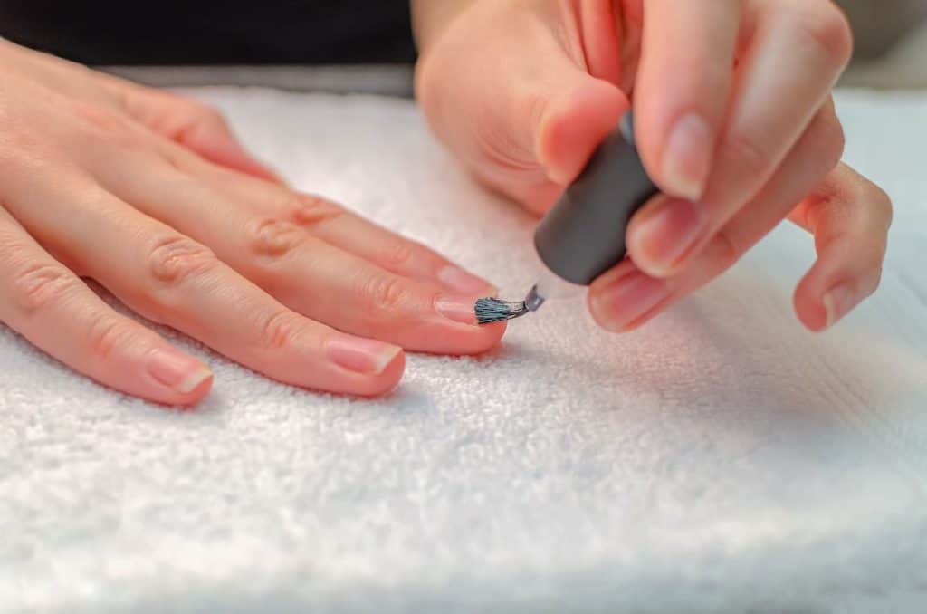 A woman using nail dehydrator on her fingernails using a black brush