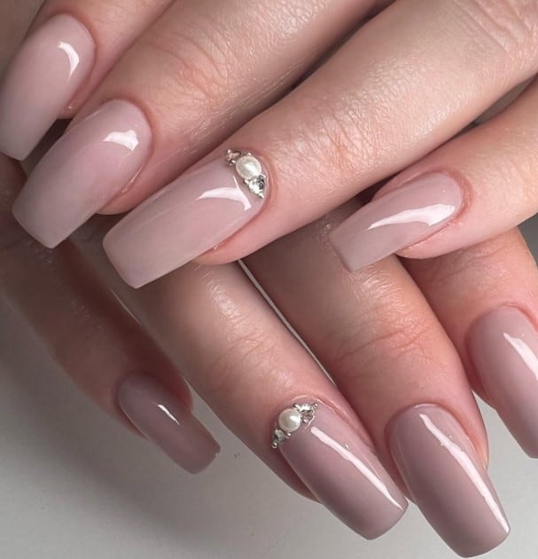 A woman's hands with nude square nails adorned with pearls and metallic accessories