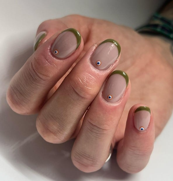 A woman's hands with pink-grey nail polish and a blue-colored bead with olive green french tips