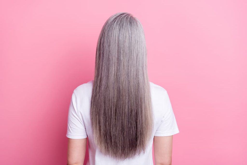 The back of a woman with long grey hair on a pink background.