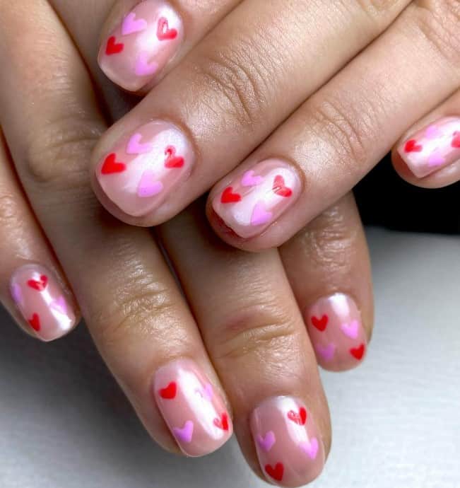 A woman with pink glazed donut nails with pink and red hearts