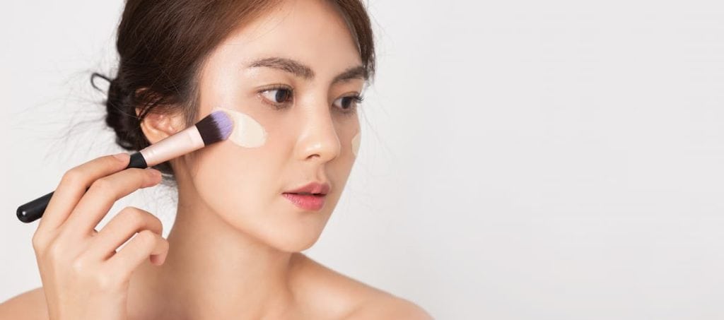 Closeup face beside of young asian woman applying foundation cream with brush to her face on banner white background