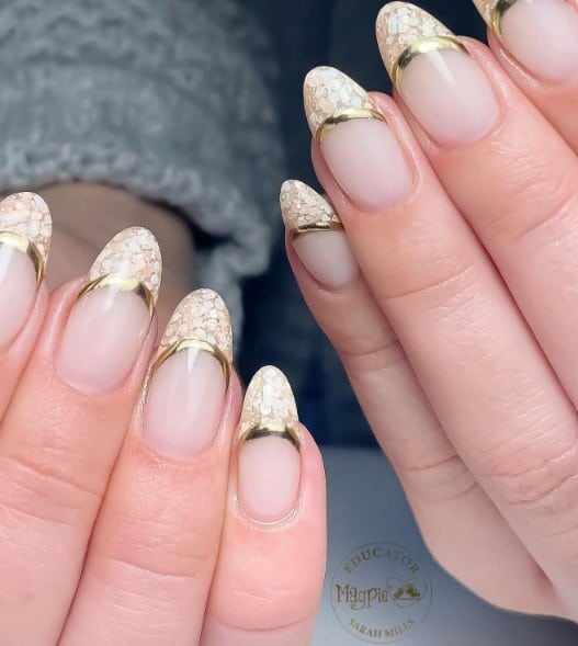 A woman's hands with deep bokeh-inspired French tips lined with gold on pale pink-colored nails.