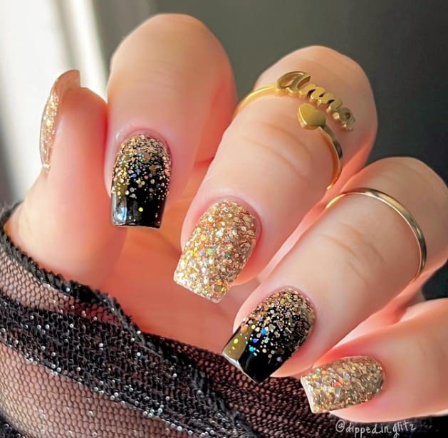 A woman with black glitter nail design features mid-length square nails full of gold glitter