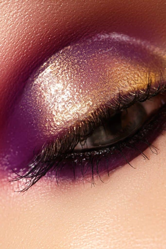 Close up of a woman's eye with purple and gold makeup.
