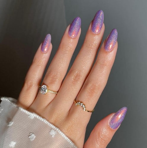 A woman's almond-shaped nails bathed in a dreamy lavender hue and embellished with a streak of peachy pink