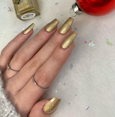 A woman's hand holding a gold nail polish