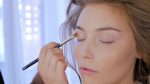 Professional makeup artist applying cream base eyeshadow primer to model's eye