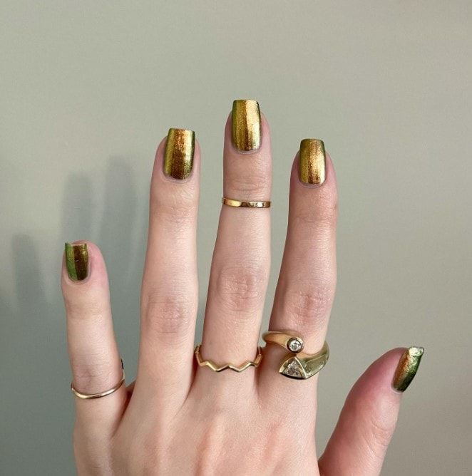 A woman's hands with gold chrome square nails are with their solid color and shiny finish