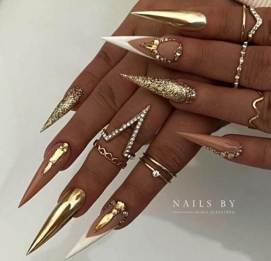 A woman's nails with glistening gold, white French tips, and peach-colored nails with gold rhinestones on top