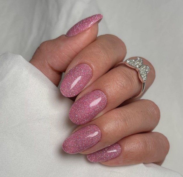 A woman's long oval nails are dipped in rose pink powder and blended with shimmering silver glitter
