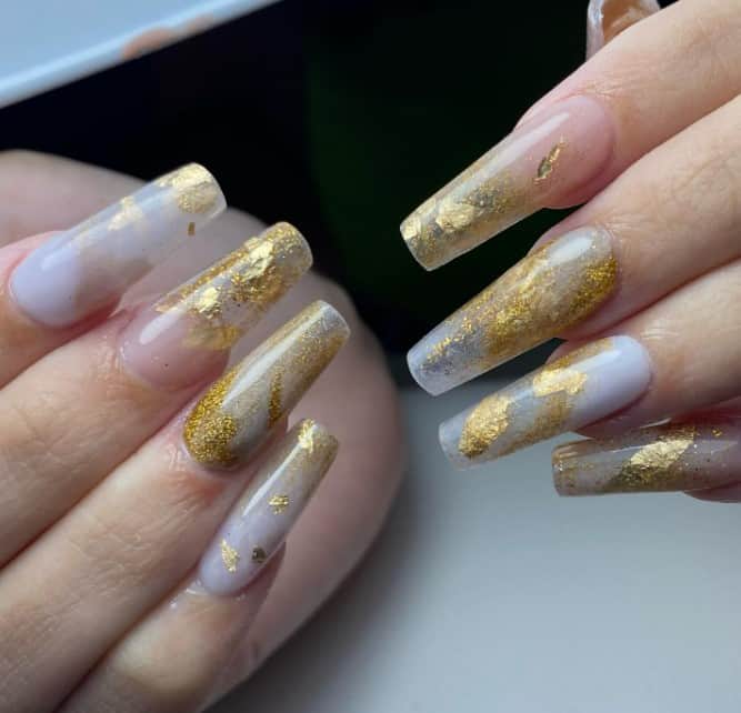 A woman's nails with milky and sheer white mani looks with spots of gold glitter and flecks of foil