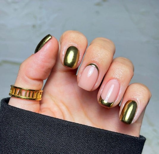 A woman's hand with two French tips on nude nails, one traditional tip with gold at the top and the other a reverse tip with gold along the bottom