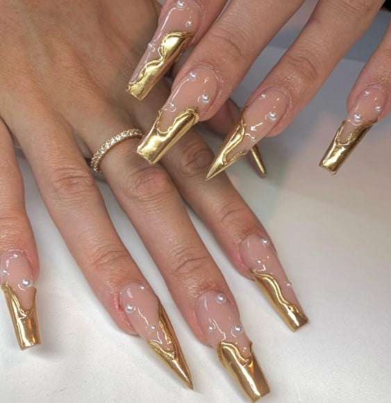 A woman's nails are decorated with clear nails with white pearls and French Tips of various sizes, making it seem like you dipped your fingers in a pot of gold.