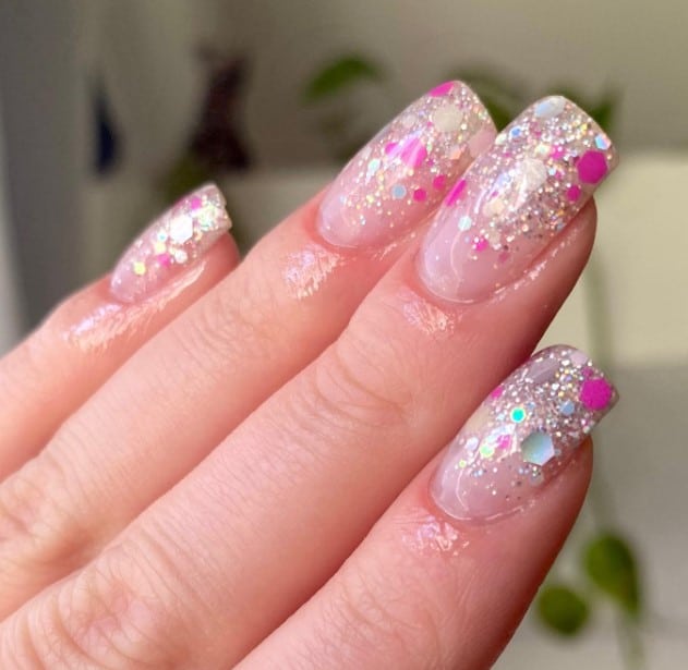 A woman's mid-length square nails decorated with an alluring cascade of fine silver glitter starting from the tips and fading away down the middle