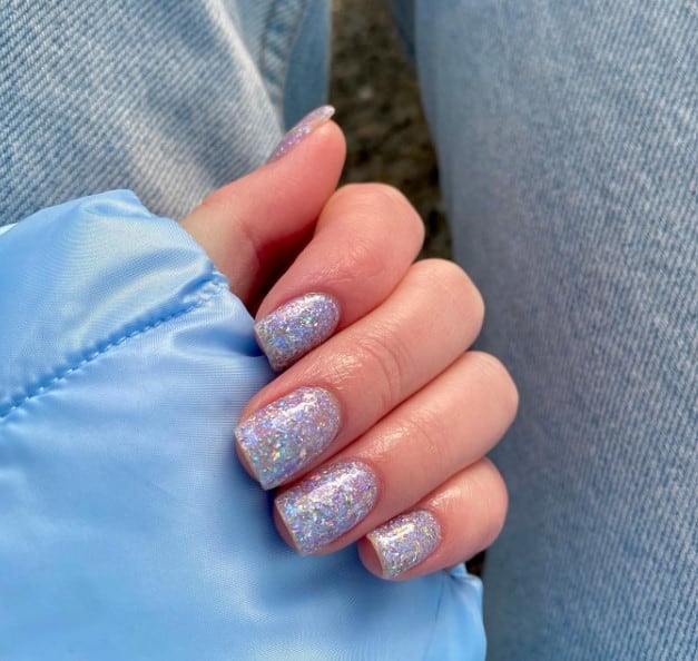 A woman's square nails glisten with fine silver glitter, casting a mesmerizing holographic spell