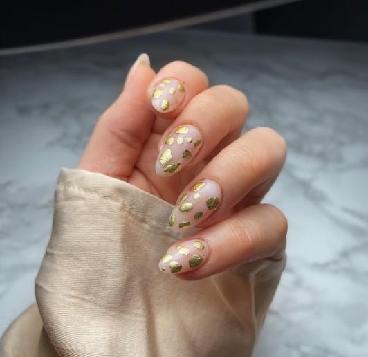 A woman's hand with foil gold flakes nails with a pale pink base look like a fun and elegant animal print