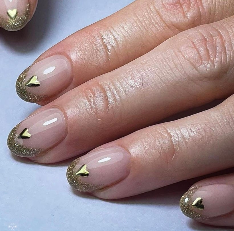 A woman's nails with glittery gold French tips over nude-colored nails