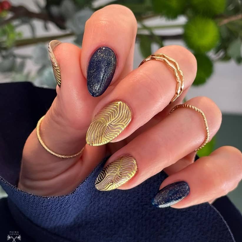 A woman's nails with blue nails sprinkled with gold dust and gold textured nails full of thin gold lines converging at the center.