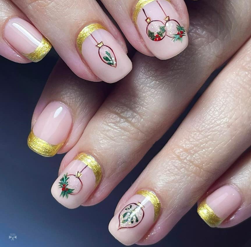 A woman's nails are decorated with regular and reverse French gold manicures with delicate drawings of Christmas tree ornaments