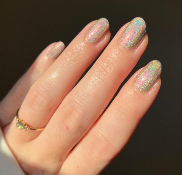 A holographic nail polish being held by a woman's hand, showcasing silver glittery nail ideas.