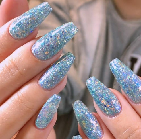 A woman's blue glitter nail design turns long coffin nails into a canvas of shimmering blue