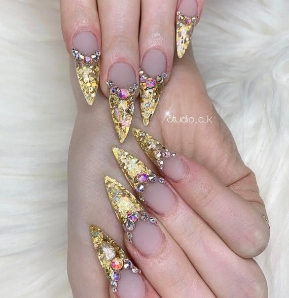 A woman's nails are decorated with French manicure that rocks pink and clear rhinestones with generous gold foil tips