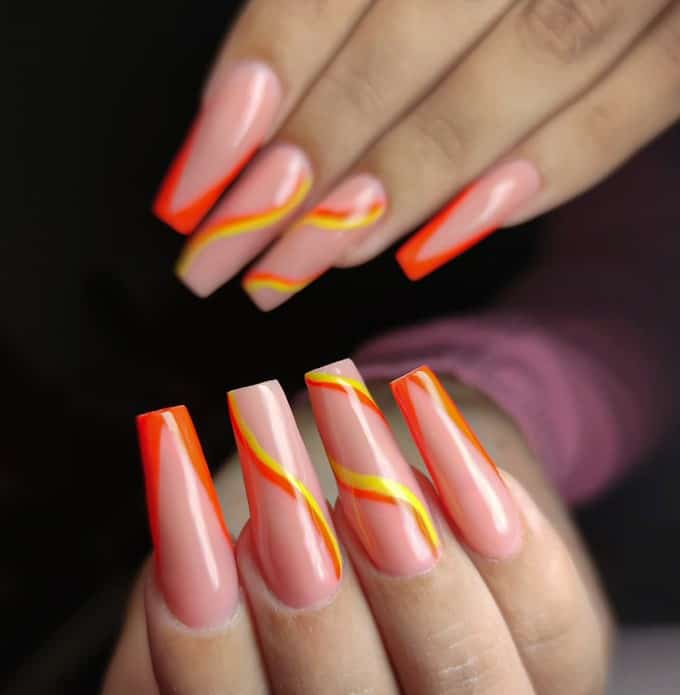 A woman's nails with  wavy lines in yellow and orange on nude nails