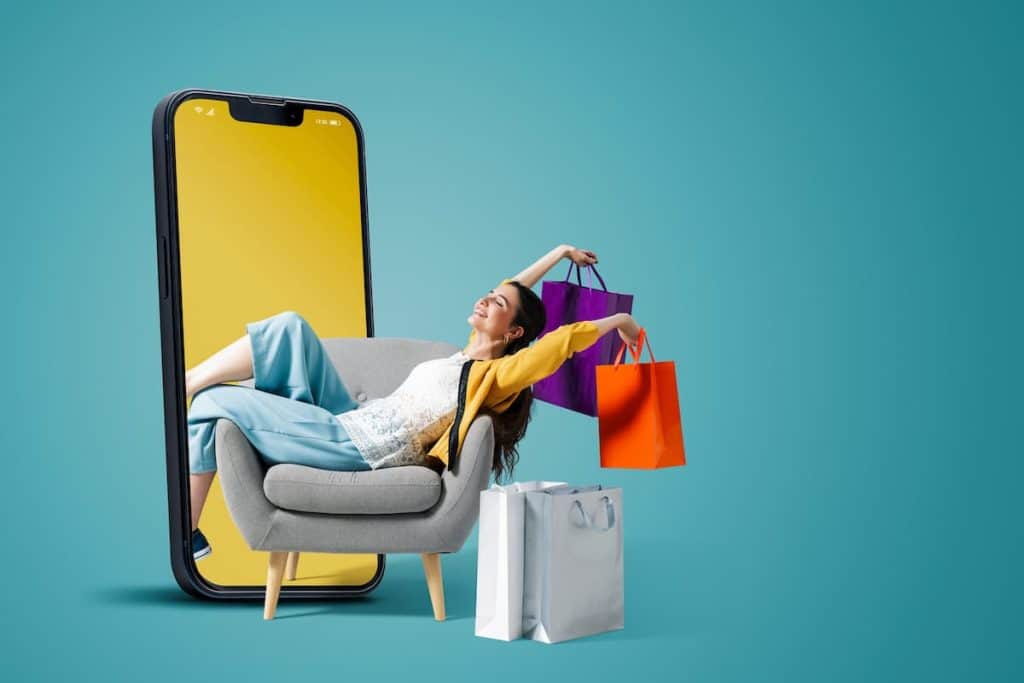 Happy fashionable young woman sitting and holding shopping bags in a smartphone