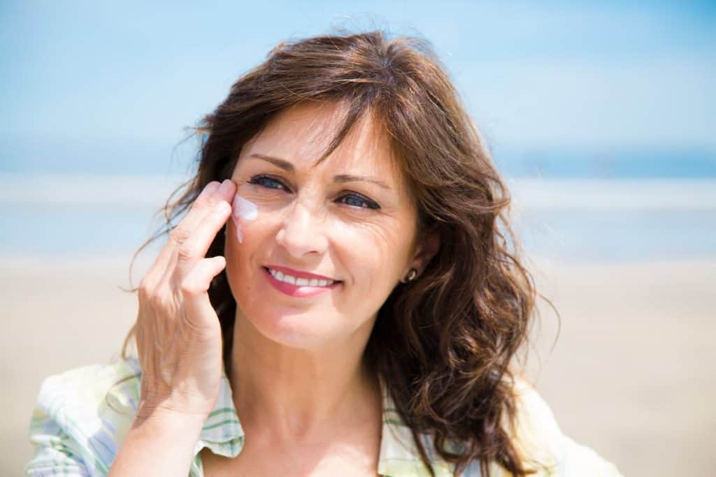 Beautiful middle aged woman applying sunscreen lotion on face on the beach
