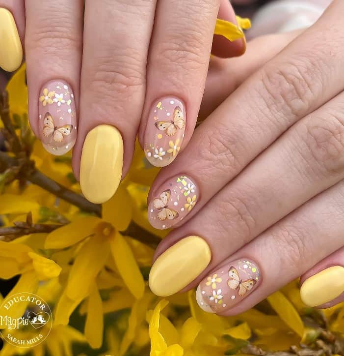 A woman's pale yellow base with nude nails and very light yellow French tips with added intricate garden-inspired nail art featuring butterflies, white and yellow flowers, and multi-color flecks
