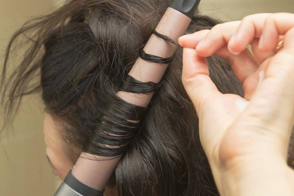A close up image of a woman using a curling iron to curl her hair.