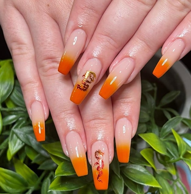 A woman's hand with orange ombré base and gold dragon designs