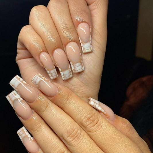 A woman's hands glamorously flaunting nude nails with brown-and-white croc print French tips
