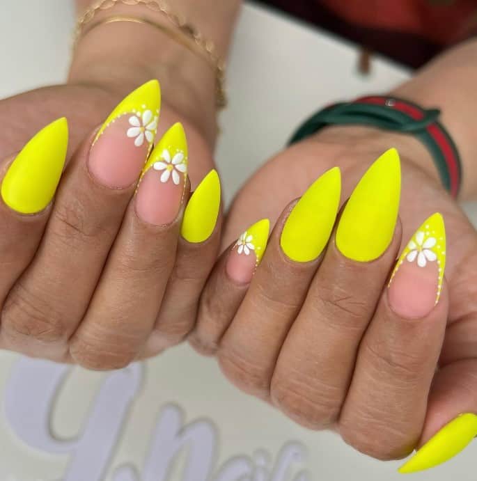 A woman's hands with neon yellow nails with nude accent nails decorated with neon French tips and white flowers outlined in micro-white dots