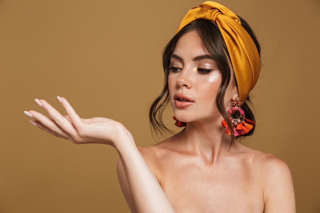 Close up beauty portrait of an attractive young topless woman wearing headband standing isolated over brown background