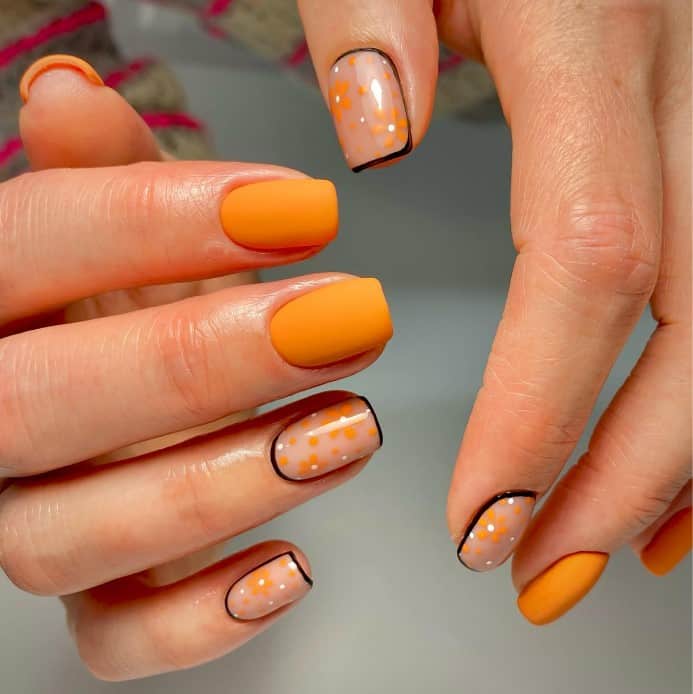 A woman's hands with matte orange nails and translucent white base with a black outline accent nails