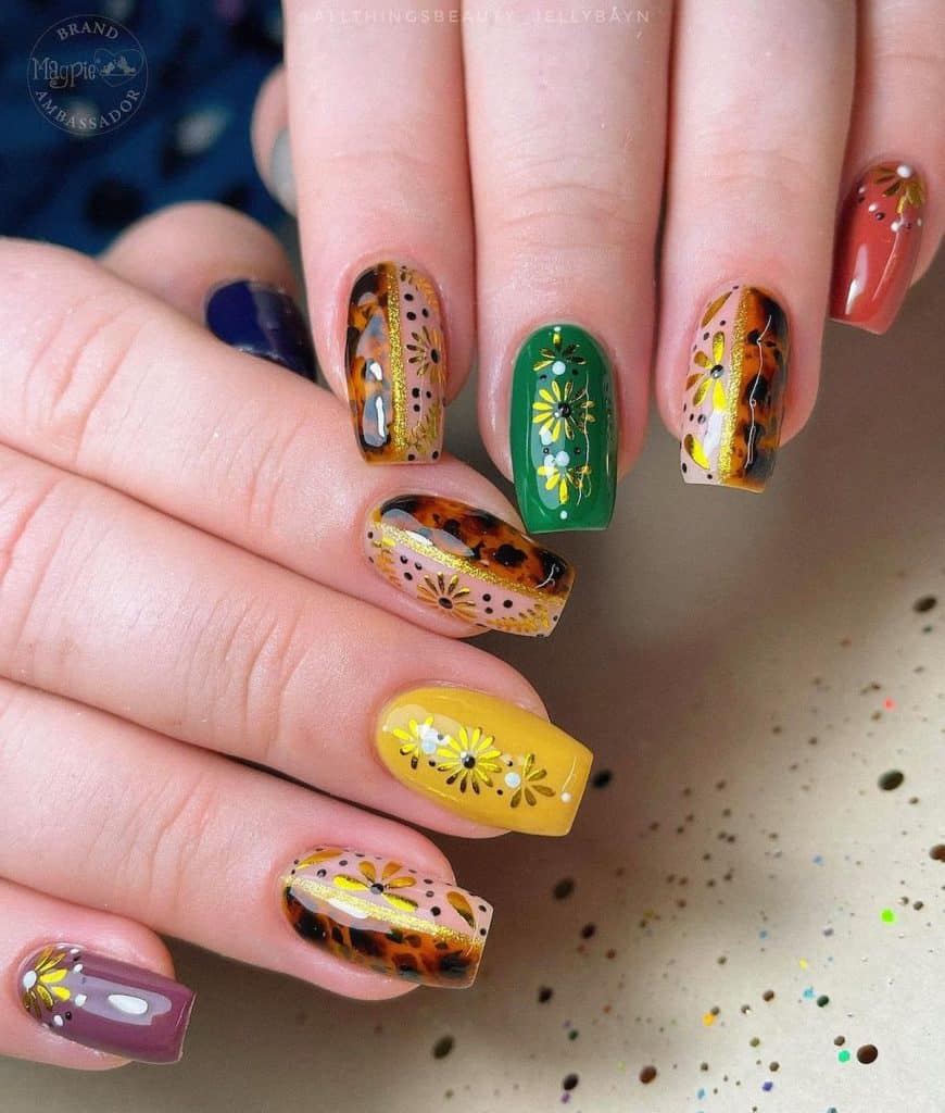 A woman's hands with nails with two alternating styles with vivid colors like purple, yellow, green, blue, and brown, decorating each with golden floral accents