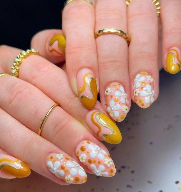 A woman's nude base nails features white flowers in varying sizes with pearl or gold centers and multicolored yellow dots