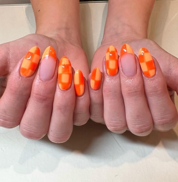 A woman's hands with orange checkered nail design in two shades
