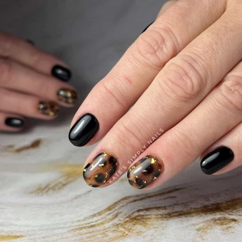 A woman's hands with oval nails painted in black, save for two that come with tortoiseshell patterns and a speckle of gold foil bits for a touch of midnight magic.
