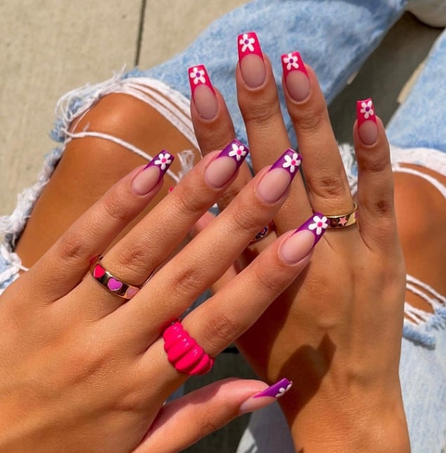 A woman's hands with pink flower nail design features one hand that flaunts French tips in regal purple while the other dazzles in hot pink